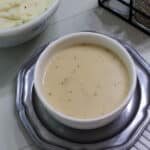 Feature image of a white bowl full of gravy sitting on a silver colored plate.