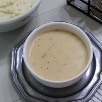 Feature image of a white bowl full of gravy sitting on a silver colored plate.
