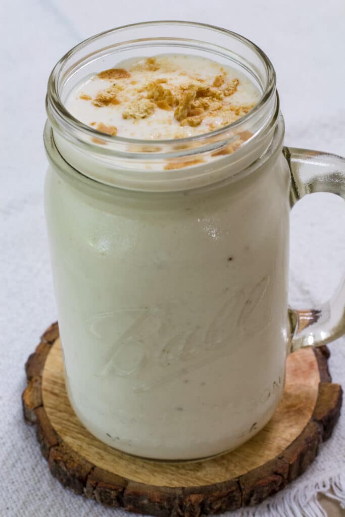 A mason jar mug full of Banana Smoothie sitting on wooden coaster.