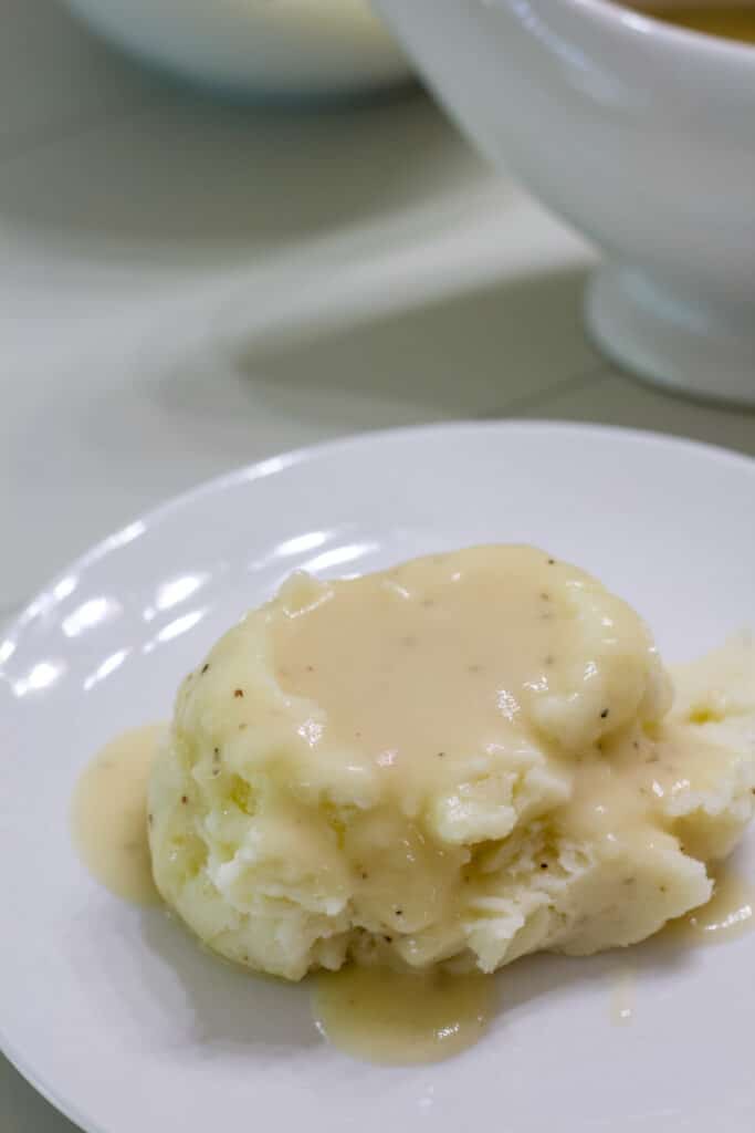 One serving of mashed potatoes topped with chicken gravy on a white plate.