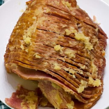 The whole spiral ham on a white plate with a green and white plaid napkin next to it.