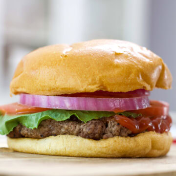 Feature image of the side view of the cooked burger on a bun with common burger toppings.