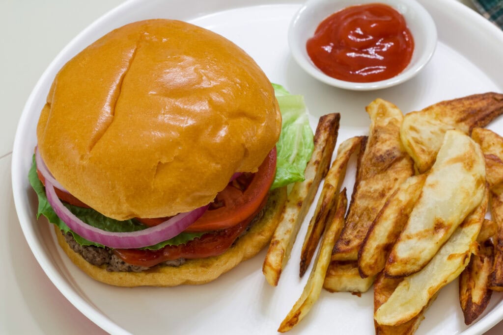 Overhead view of a hamburger, fries, and small bowl of ketchup on a white platter.