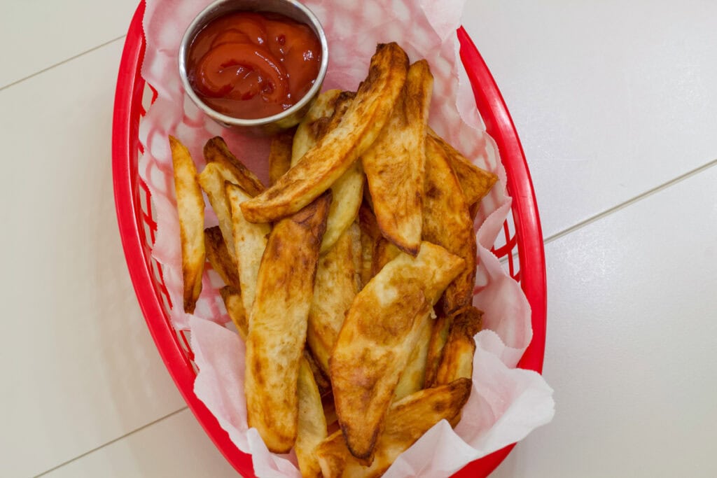 A small red parchment paper lined basket filled with cooked steak fries.