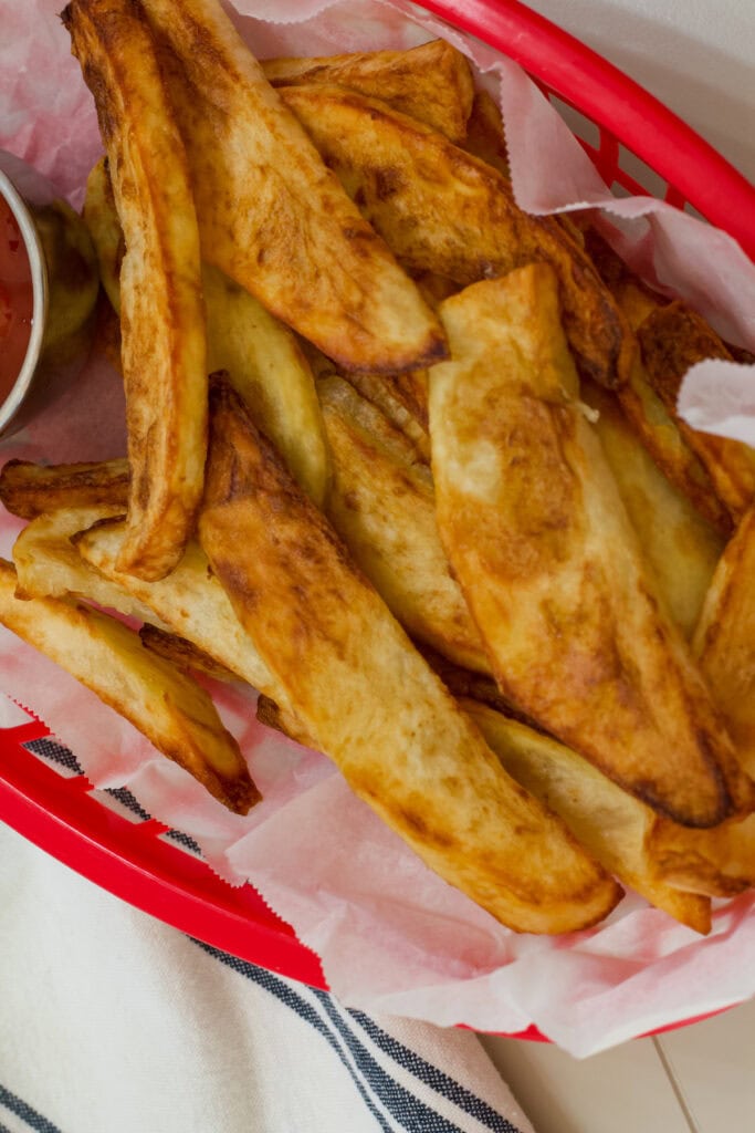 Close up shot of many cooked steak fries in a parchment paper lined basket.