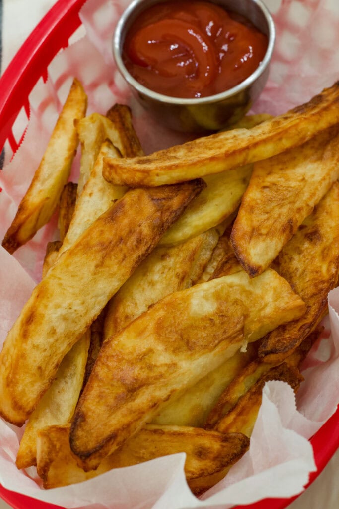 Overhead view of air fryer steak fries ready to be served in a red restaurant style red basket.