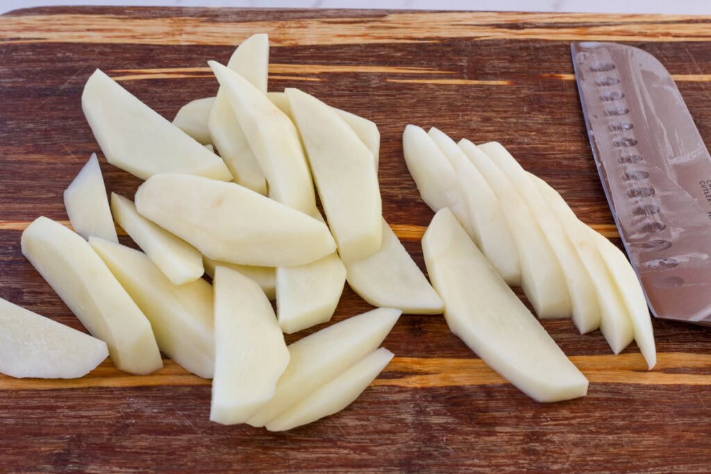 A wooden cutting board with the steak fries cut to illustrate how to cut them.