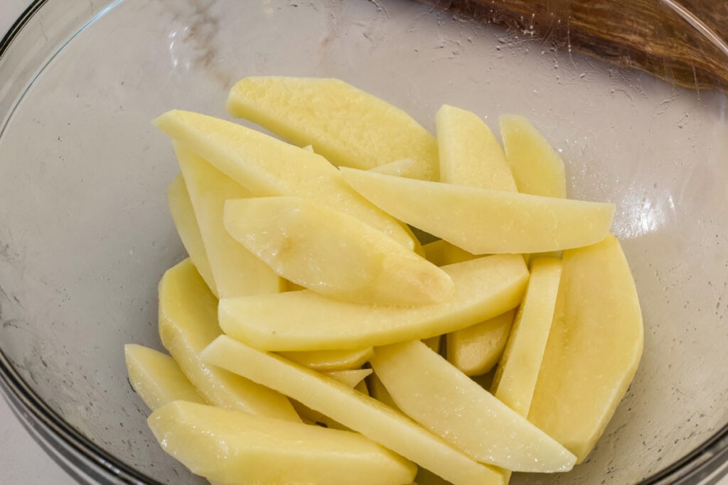 The cut raw potatoes in a large bowl after they were tossed in canola oil and salt, ready to go in the air fryer.
