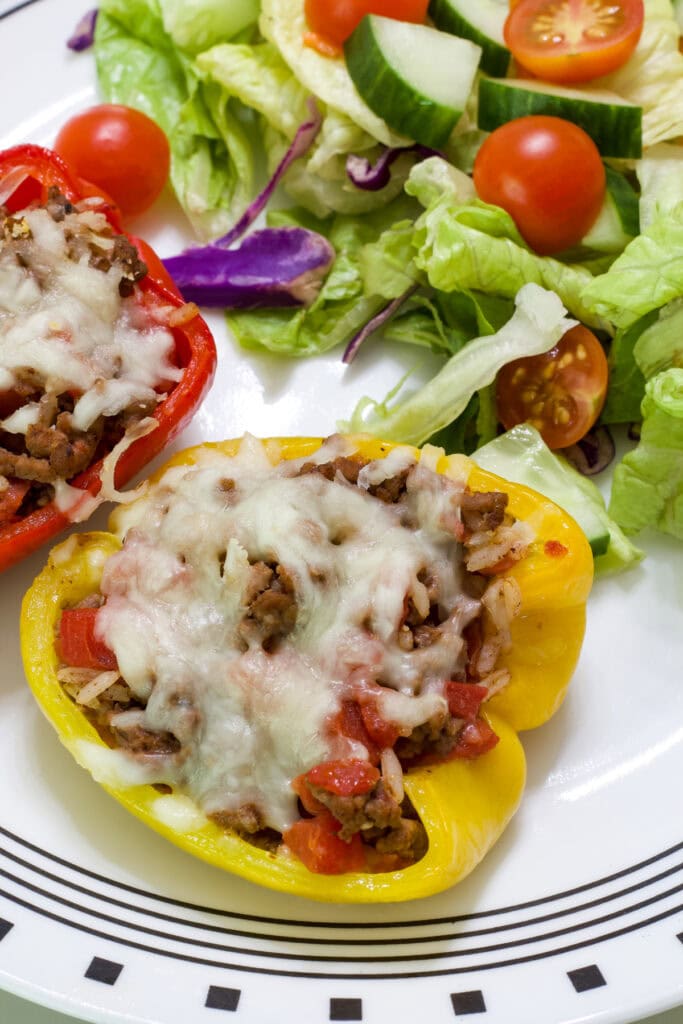 Two stuffed pepper halves on a plate with a side salad.