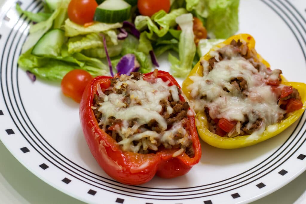 One baked red and one baked yellow pepper half on a plate with a side salad.