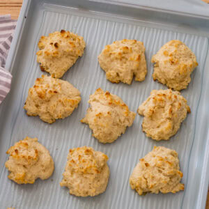 Feature image of several baked Light Yogurt Drop Biscuits on a light turquoise colored sheet pan.