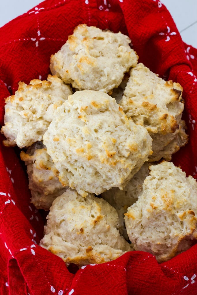 several baked biscuits in a basket lined with a red and white cloth napkin.