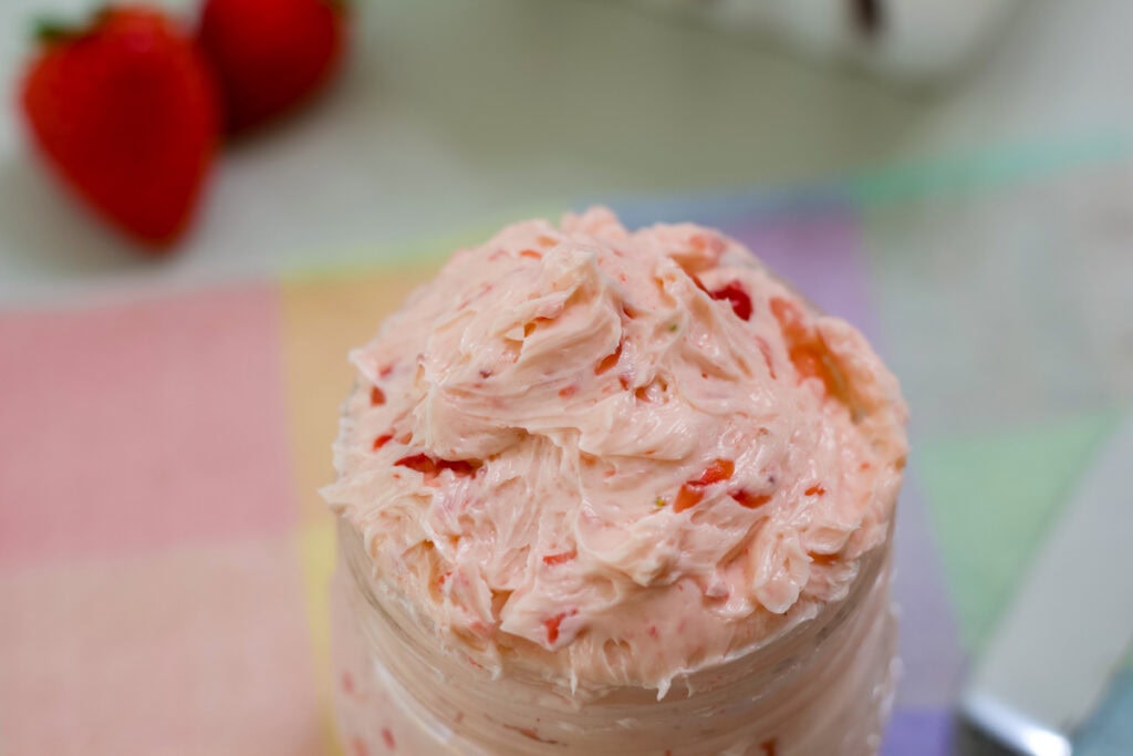 Overhead view of the top of the Whipped Strawberry Honey Butter filled jar with a couple of strawberries next to it.