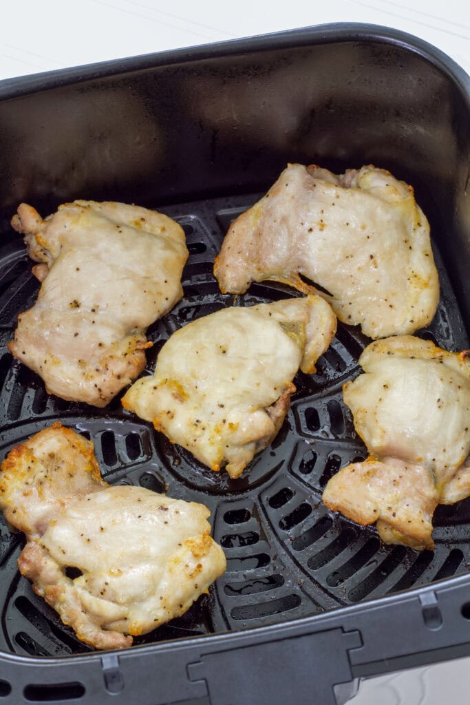 Five boneless skinless chicken thighs in the air fryer basket after they have been cooked.