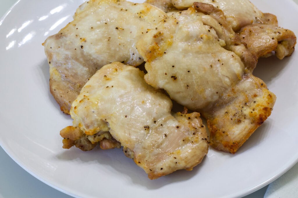 Five cooked air fryer chicken thighs on a white plate ready to be served.