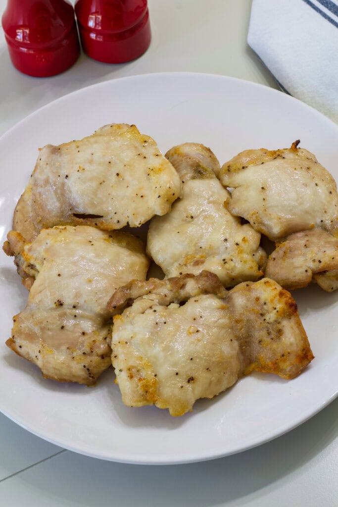 Five chicken thighs that were cooked in the air fryer on a white plate.