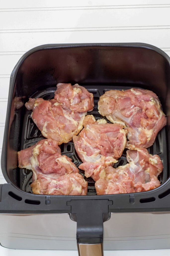 Five raw chicken thighs that have been coated in canola oil and seasonings ready to be cooked.