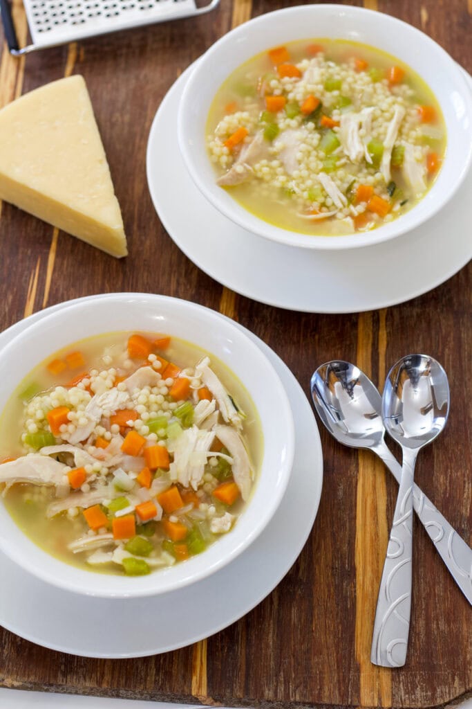 Two bowls of soup, a wedge of parmesan cheese and two spoons.