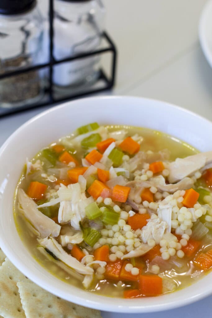 Very close up shot of a bowl of chicken pastina soup with a few crackers next to it.