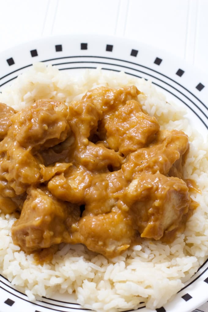 A black and white plate with one serving of peanut butter chicken on a bed of white rice.