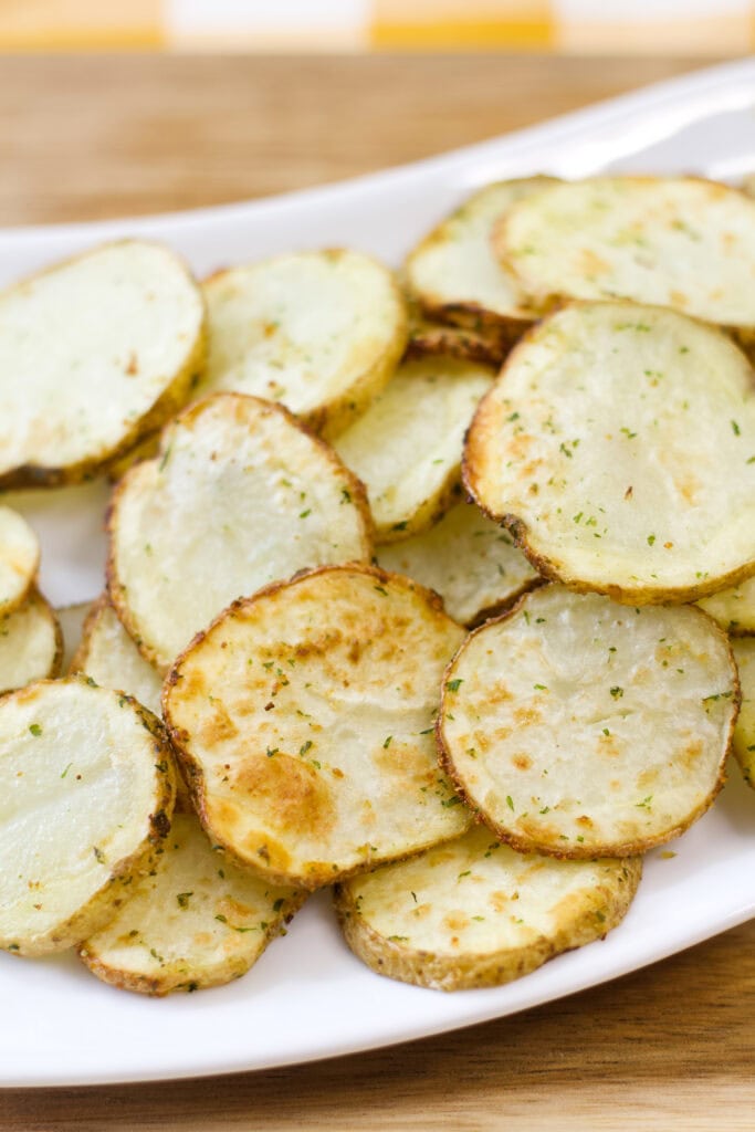 Close up of several servings of air fried sliced potatoes on a white serving plate.