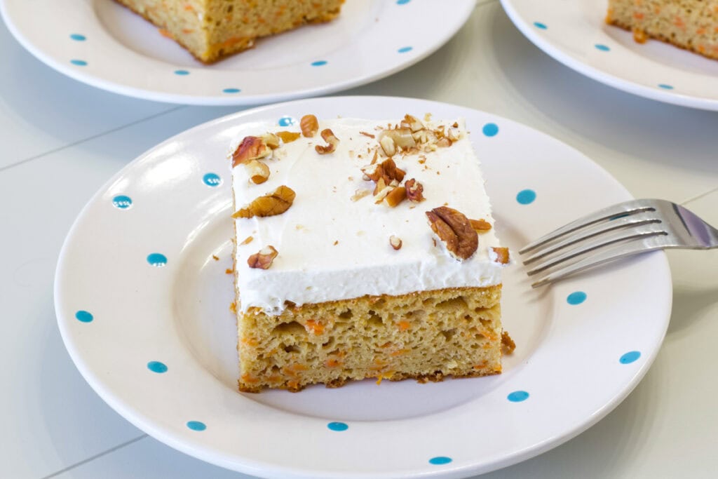 One piece of carrot cake topped with cream cheese frosting on a white plate that has blue polka dots.
