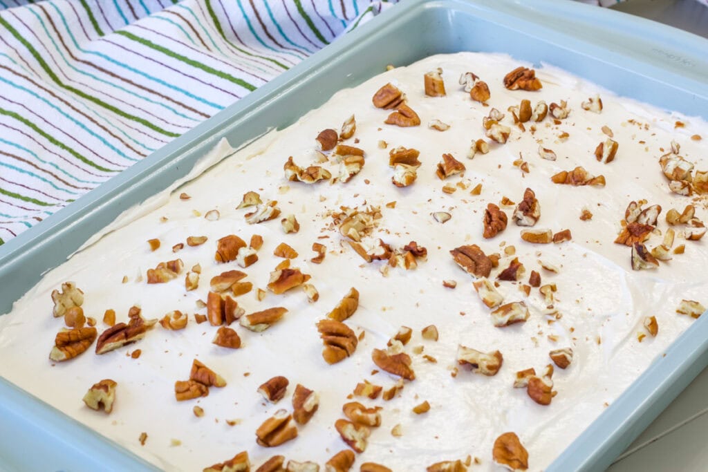 Side view of the frosted uncut cake that's been topped with chopped pecans.