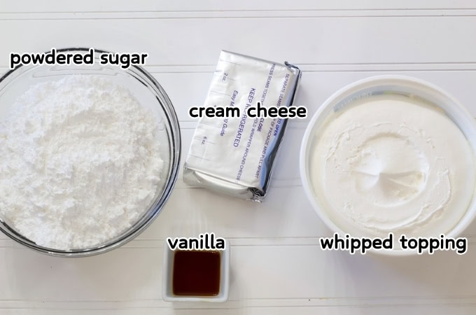 A bowl of powdered sugar, a brick of cream cheese, a bowl of whipped topping and small bowl of vanilla that's needed to make the Lazy Whipped Cream Cheese Frosting recipe.