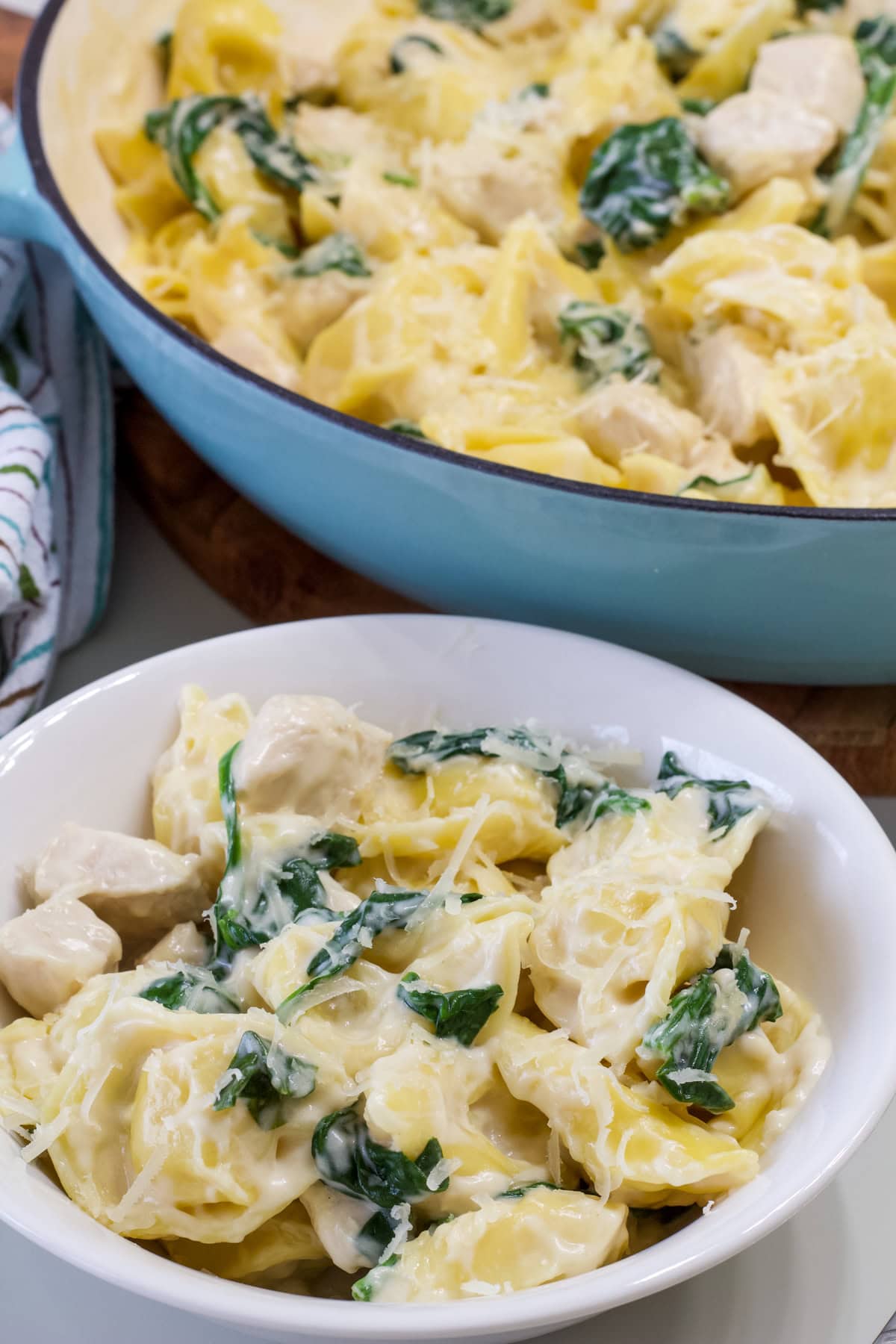 A serving of chicken tortellini in a white bowl in the foreground and the pan with the remaining pasta in the background.