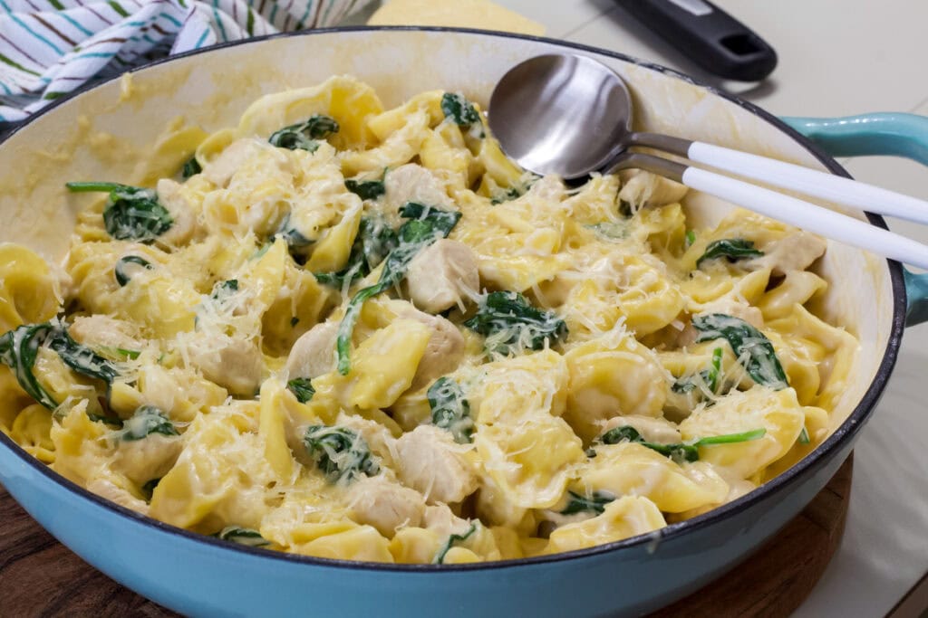 Side shot of the entire batch of One Pan Chicken and Tortellini Alfredo in a blue skillet.