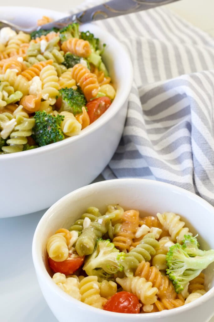 One serving of rainbow pasta salad in the foreground and the serving bowl with the rest in the background.