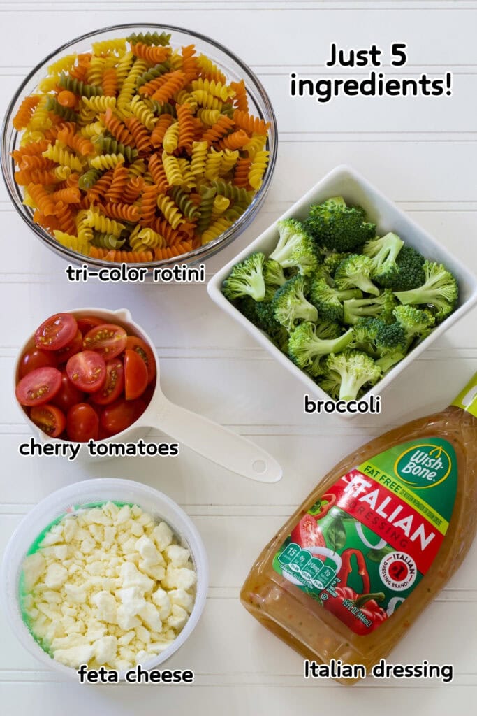 The raw pasta, chopped broccoli, halved cherry tomatoes, feta cheese and a bottle of Italian dressing ready to make the Rainbow Pasta Salad Recipe.