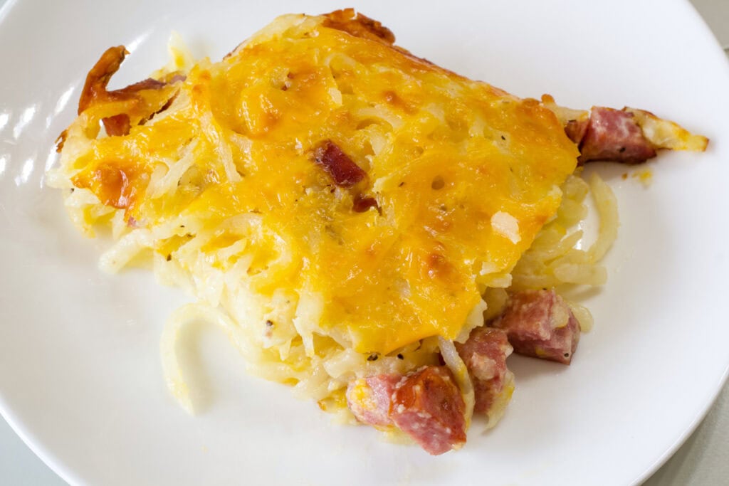One serving of cheesy hash brown casserole on a white plate.