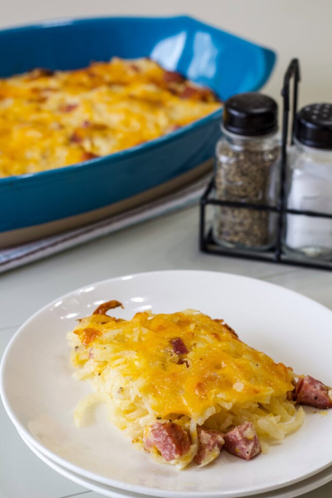 One serving of casserole on a white plate in the foreground and the baking dish with the remaining casserole in the background.