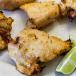 Feature image of several Air Fryer Honey Lime Chicken thighs on a white plate with lime wedges.