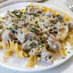 Feature image of a serving of beef stroganoff over egg noodles topped with chives.