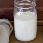 Feature image of a large mason jar filled with Homemade Caramel Coffee Creamer, there's a tan colored napkin next to it.
