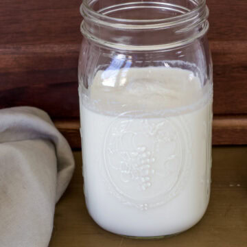 Feature image of a large mason jar filled with Homemade Caramel Coffee Creamer, there's a tan colored napkin next to it.