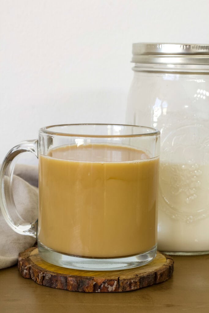 A cup of coffee that has the homemade creamer in it sitting next to a mason jar with more creamer in it.