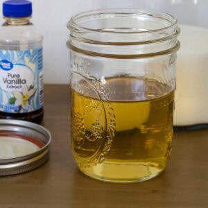 Close up of the Homemade Caramel Syrup for Coffee in a jar with a bottle of Great Value vanilla and a container of sugar in the background.