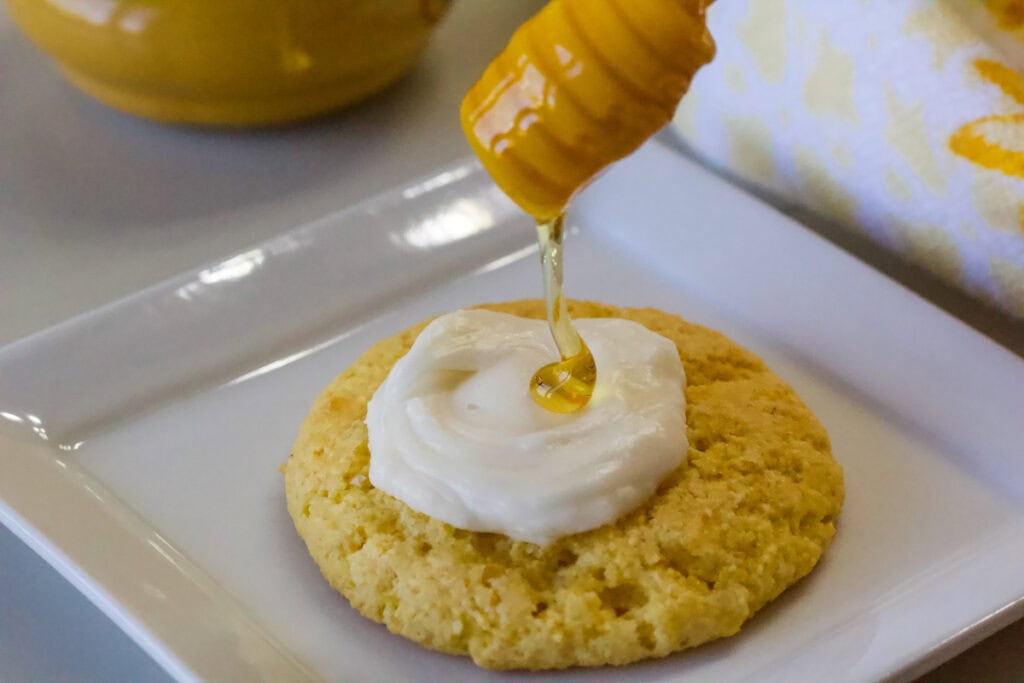 One cornbread cookie with a drizzle of honey being put on the honey buttercream that's on the top of the cookie.