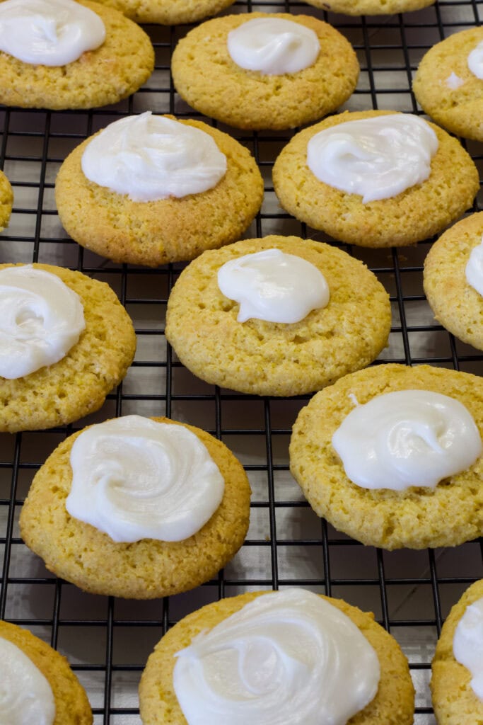 Several Jiffy Cornbread Cookies with frosting on them on a black wire cooling rack.