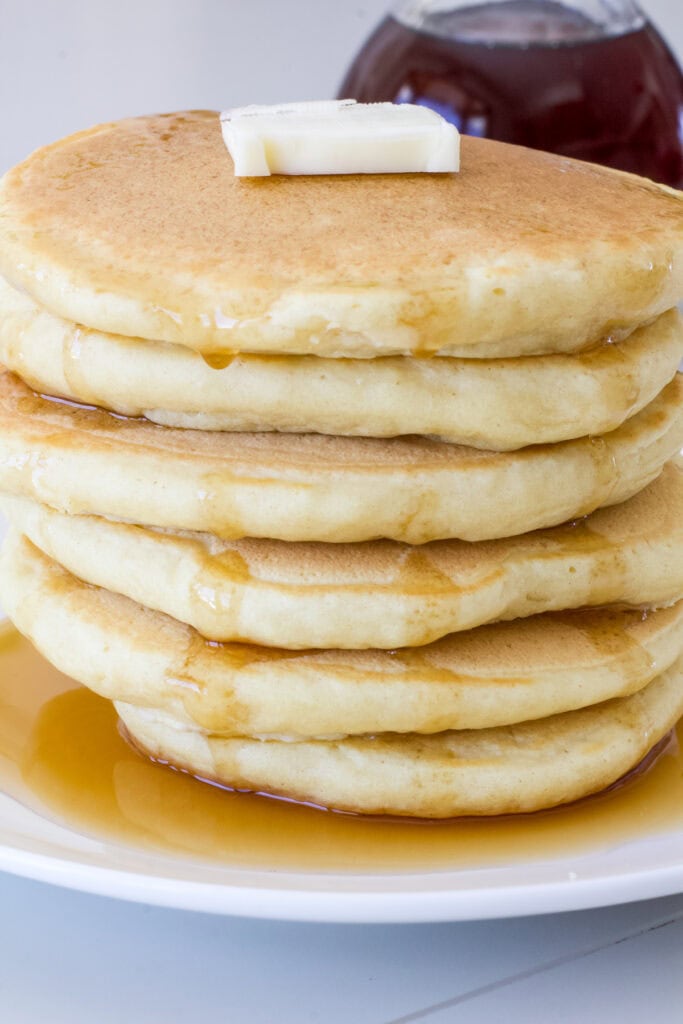 A stack of six pancakes with a pat of butter and syrup poured down over them.