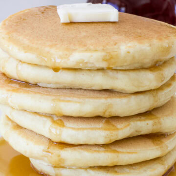 Feature image of the side view of a stack of six pancakes with syrup running down them.