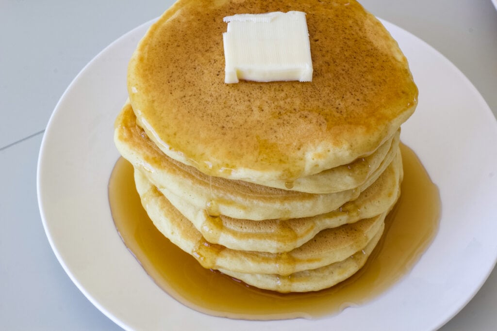 Overhead shot of a stack of six pancakes topped with butter and syrup.
