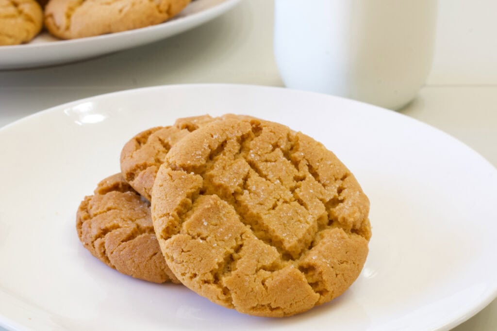 Three baked peanut butter cookies on a white plate, one is leaning on the other two.