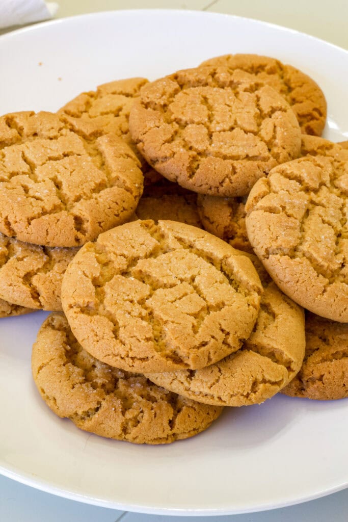 A large white plate with many Old-Fashioned Chewy Peanut Butter Cookies stacked on it.