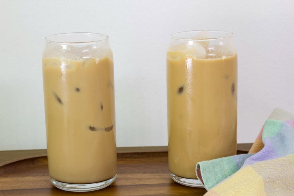 Two glasses of Dunkin French Vanilla Swirl Iced Coffee on a wooden tray.