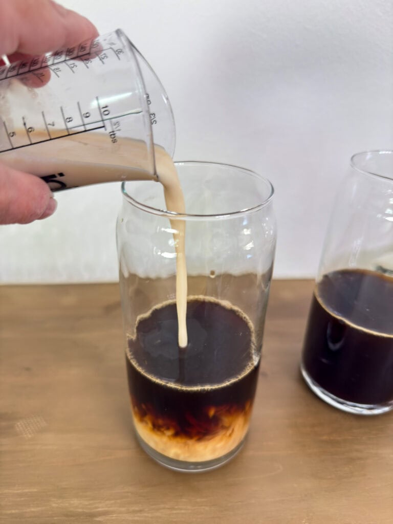 A glass with strong black coffee in it and the French vanilla swirl is being poured into it.