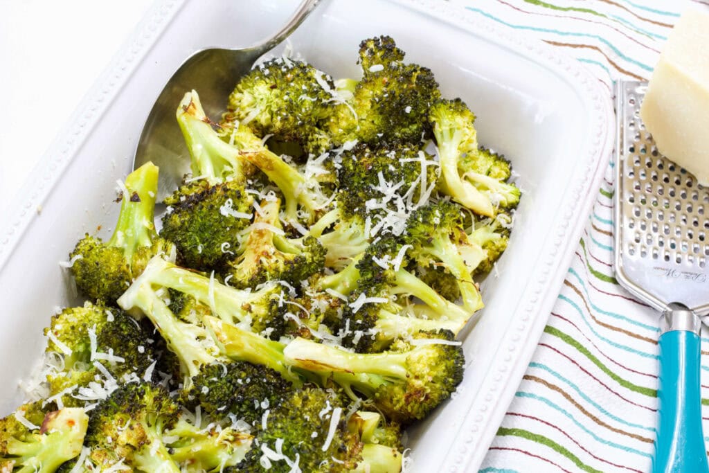 A serving dish filled with the Easy Italian Roasted Broccoli and a grater with a block of parmesan cheese next to it.